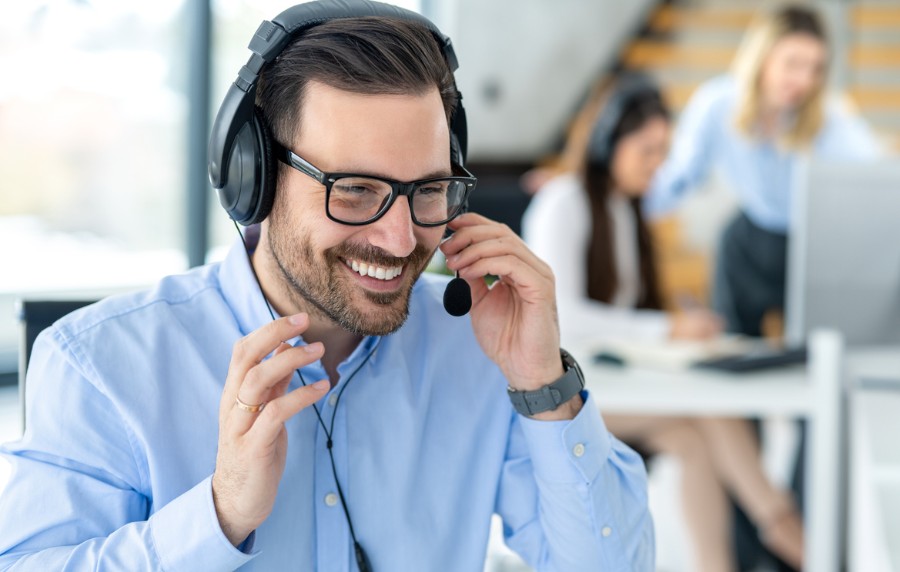 Ein Mann im Hemd trägt ein Headset und lacht beim Telefonieren.