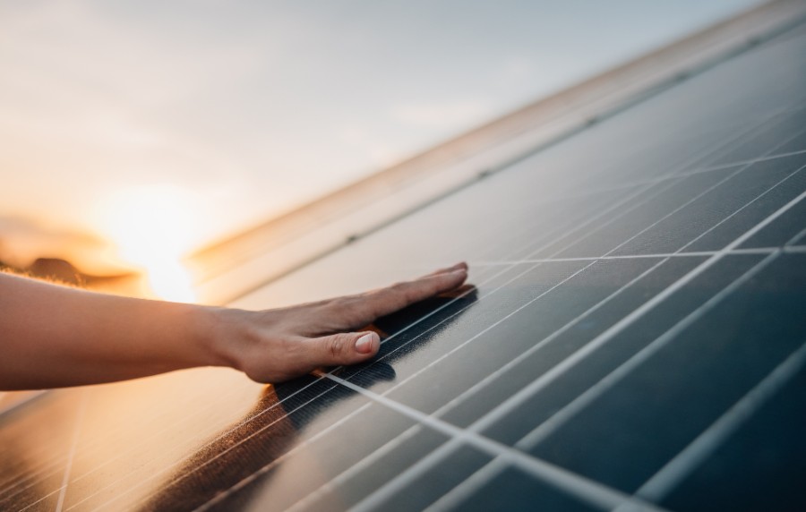 Eine Hand streicht über einen Solaranlage, Sonnenuntergang im Hintergrund